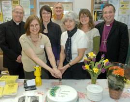 Two people cutting a cake while the others look on.