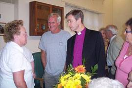 Bishop Tim addressing a group of three people, with others seen in the background.