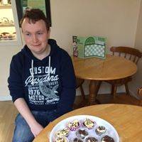 Marcus sat at a table in the cafe with a plate of decorated buns sat on the table.